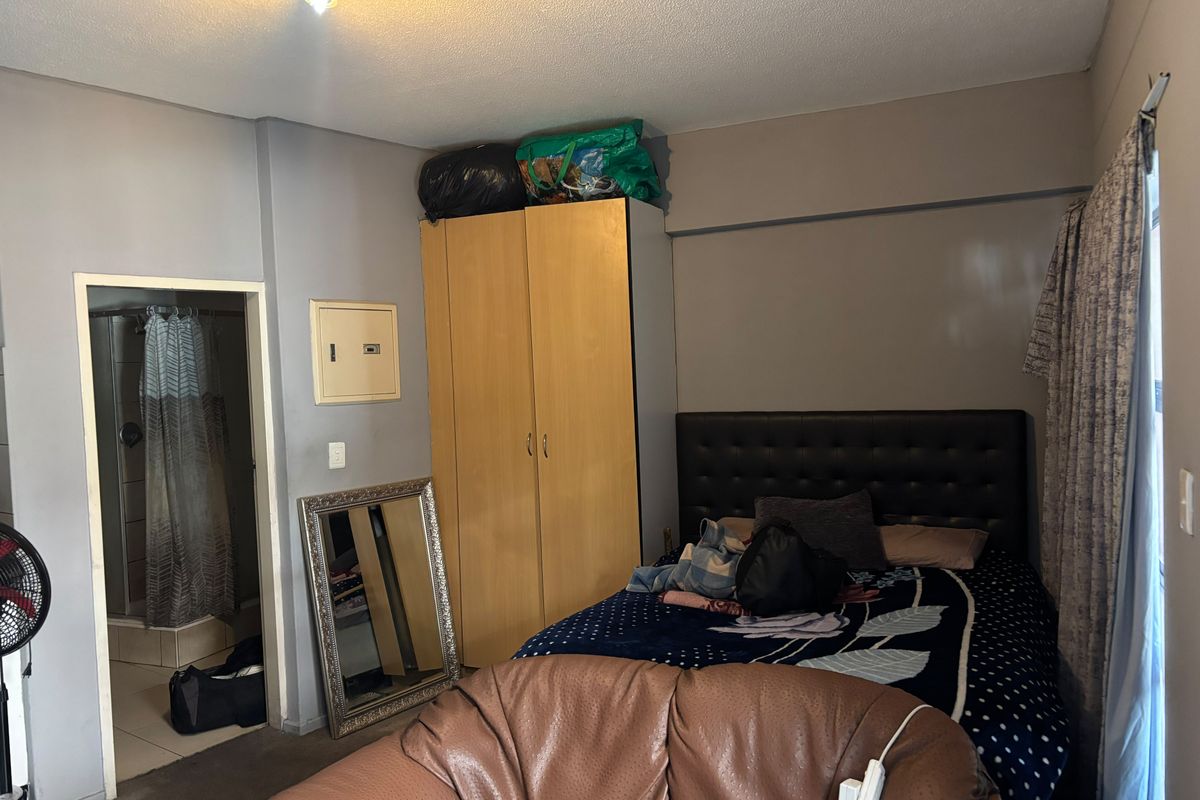 Bedroom featuring a built-in wardrobe, en-suite bathroom access, and neutral wall finishes, offering a functional layout in need of cosmetic updates.