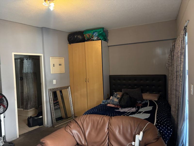 Bedroom featuring a built-in wardrobe, en-suite bathroom access, and neutral wall finishes, offering a functional layout in need of cosmetic updates.