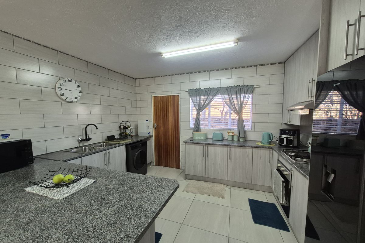 A functional kitchen featuring light wood-grain cabinetry, granite countertops, a tiled backsplash, and integrated appliances including an oven and hob.