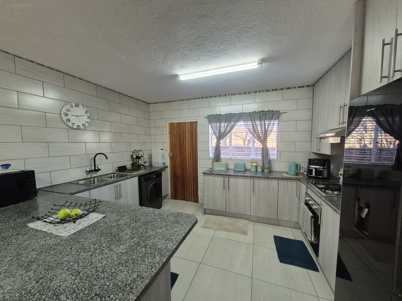 A functional kitchen featuring light wood-grain cabinetry, granite countertops, a tiled backsplash, and integrated appliances including an oven and hob.