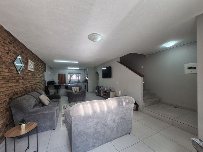Open-plan living area featuring an exposed brick wall, tiled flooring, and an integrated kitchen with a breakfast counter, leading to an internal staircase.