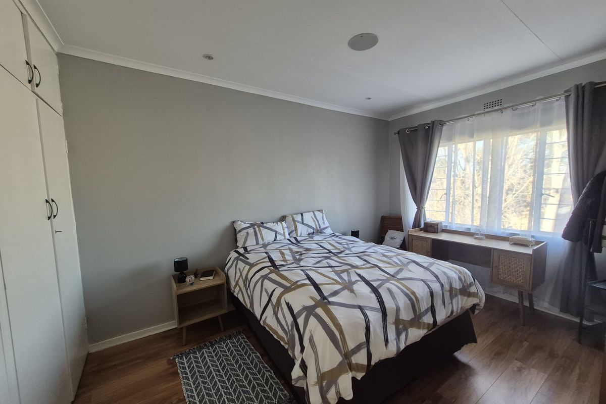 A well-maintained bedroom featuring laminate flooring, built-in cupboards, and large windows with security bars, offering a comfortable and functional living space.