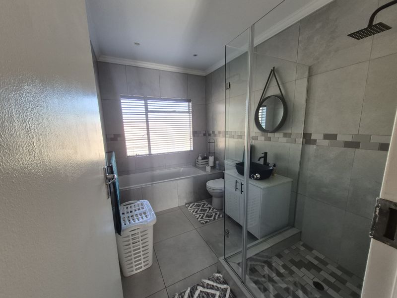 Modern bathroom featuring a glass-enclosed shower with rain head, built-in bathtub, vanity cabinet with basin, and neutral floor-to-ceiling tiling.