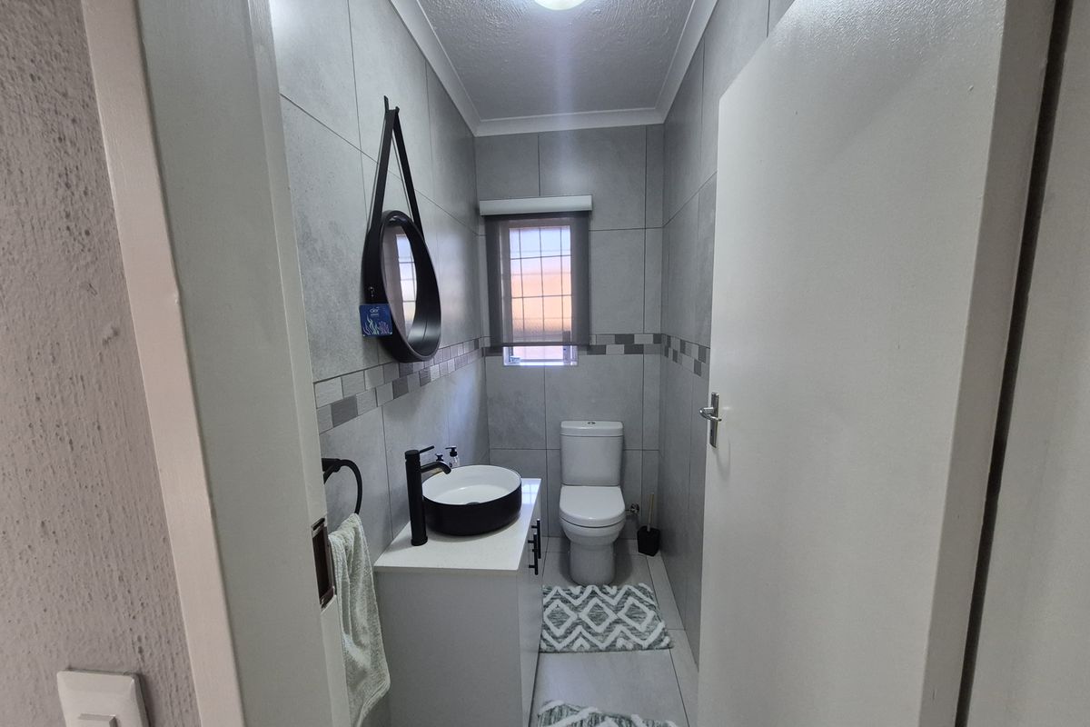 A modern guest bathroom featuring grey wall tiles, a white vanity cabinet with a black vessel sink, and a standard toilet.