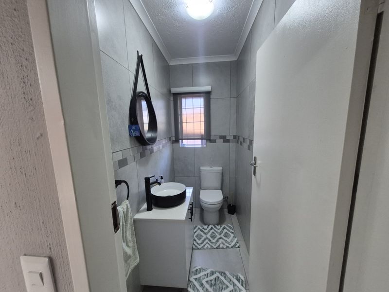 A modern guest bathroom featuring grey wall tiles, a white vanity cabinet with a black vessel sink, and a standard toilet.