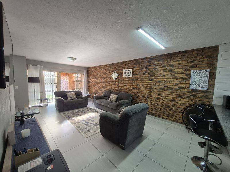 Open-plan living area featuring a prominent exposed brick feature wall, tiled flooring, and direct access to the outdoor patio through a sliding security door.