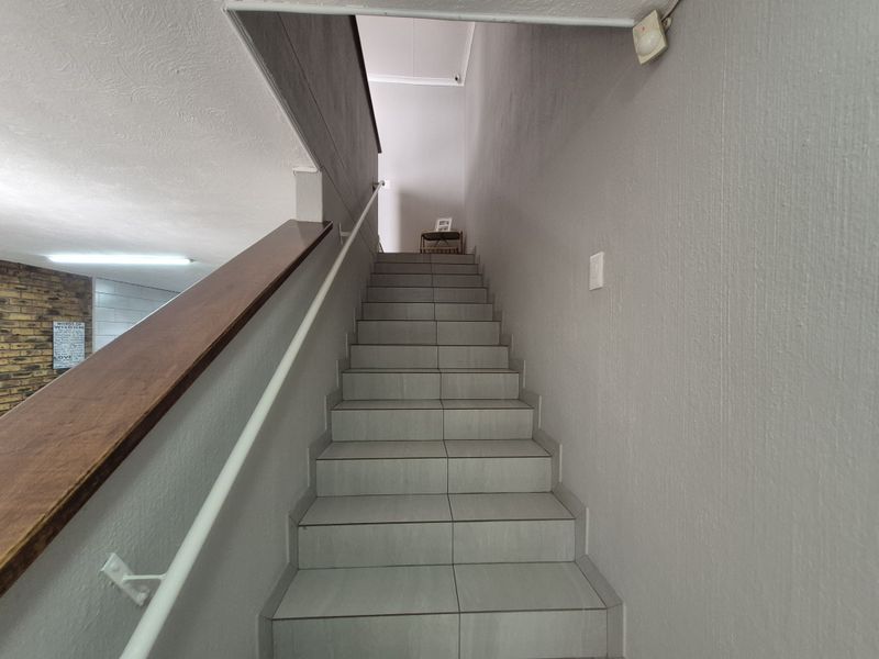 A clean, tiled staircase featuring a timber handrail and metal balustrade, providing access between levels in the townhouse.