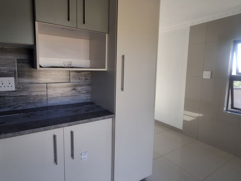 A modern, empty kitchen area featuring neutral-toned built-in cabinetry, stone-look laminate countertops, a decorative tiled backsplash, and polished floor tiles.