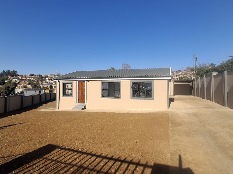 Front view of a modern single-story house featuring a concrete driveway, carport, and perimeter walling on a spacious plot.