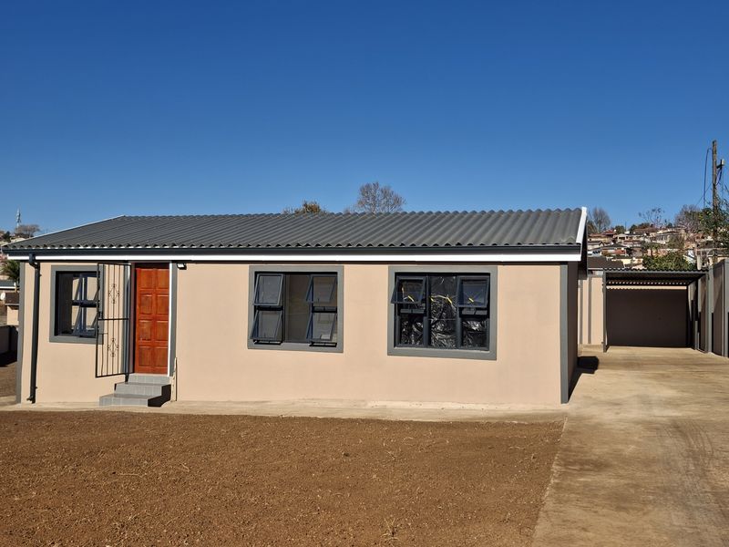Front view of a modern single-story house featuring a corrugated roof, aluminium windows, and an attached carport with a concrete driveway.