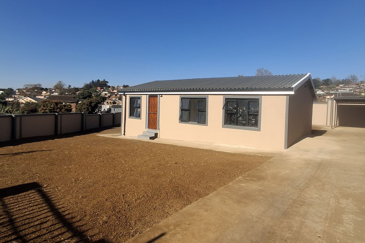 A view of the rear exterior of the house featuring a concrete driveway, perimeter wall, and an unlandscaped garden area.