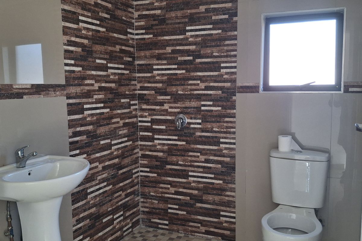 A functional bathroom featuring a pedestal basin, toilet, and a tiled shower enclosure with decorative wall accents.
