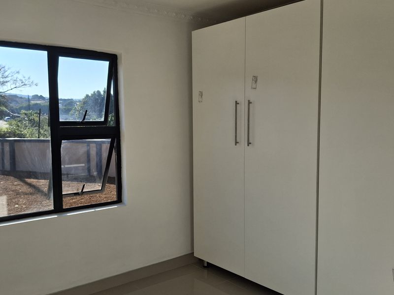 A bright, empty bedroom featuring modern tiled flooring, white built-in cupboards, and an aluminium window frame with a view.