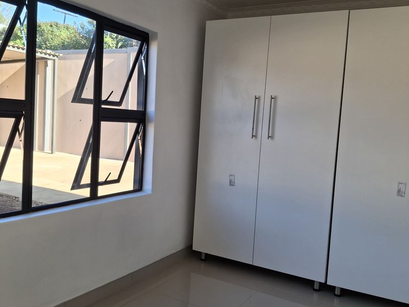 A bright, empty bedroom featuring modern tiled flooring, built-in cupboards, and large aluminium-framed windows providing natural light.