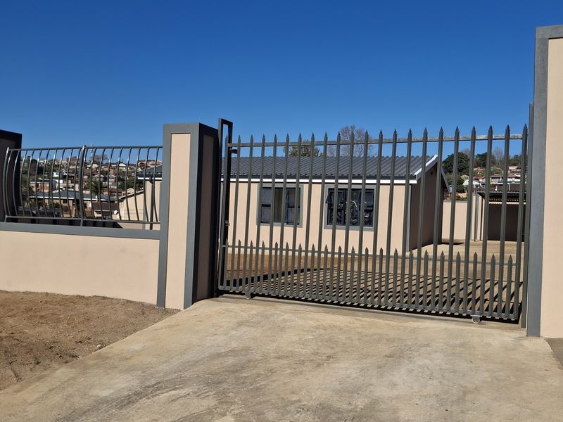 A secure front entrance featuring a modern sliding metal gate, concrete driveway, and perimeter walling with integrated metal fencing.