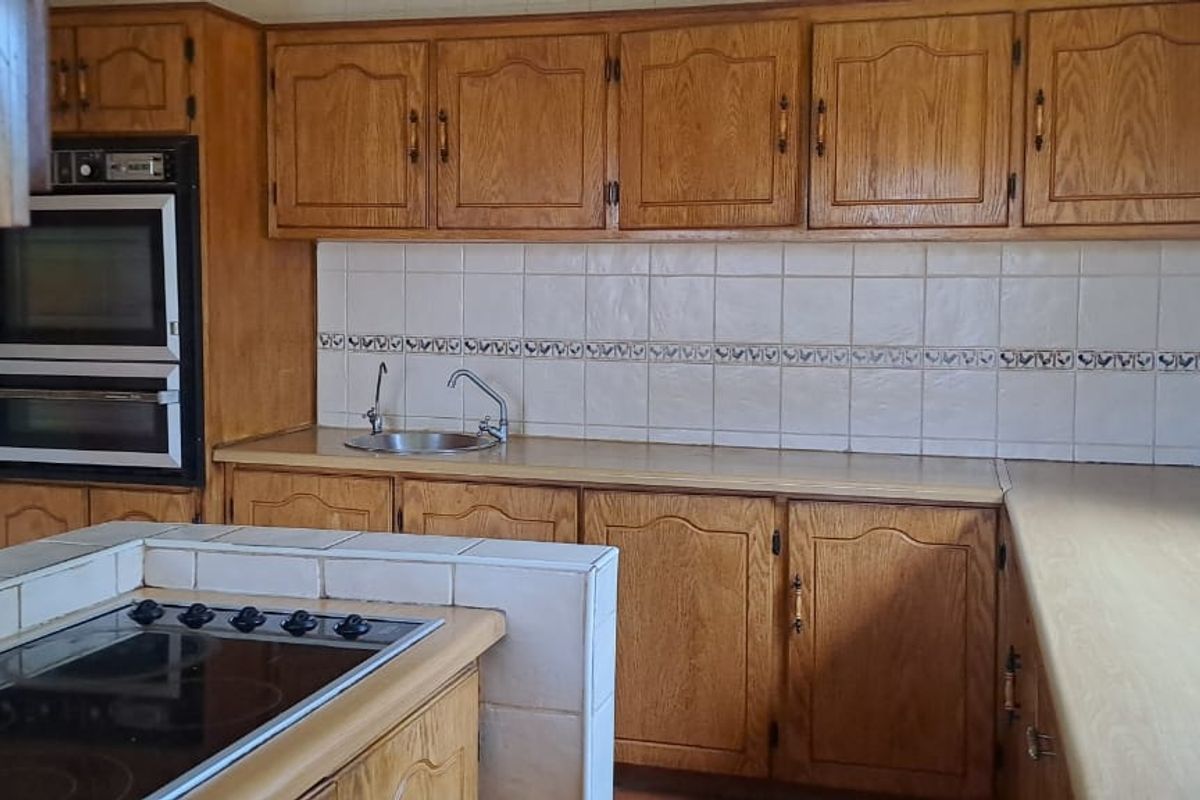 A dated kitchen featuring wooden cabinetry, tiled backsplash, built-in oven, and an electric hob set into a tiled island counter.
