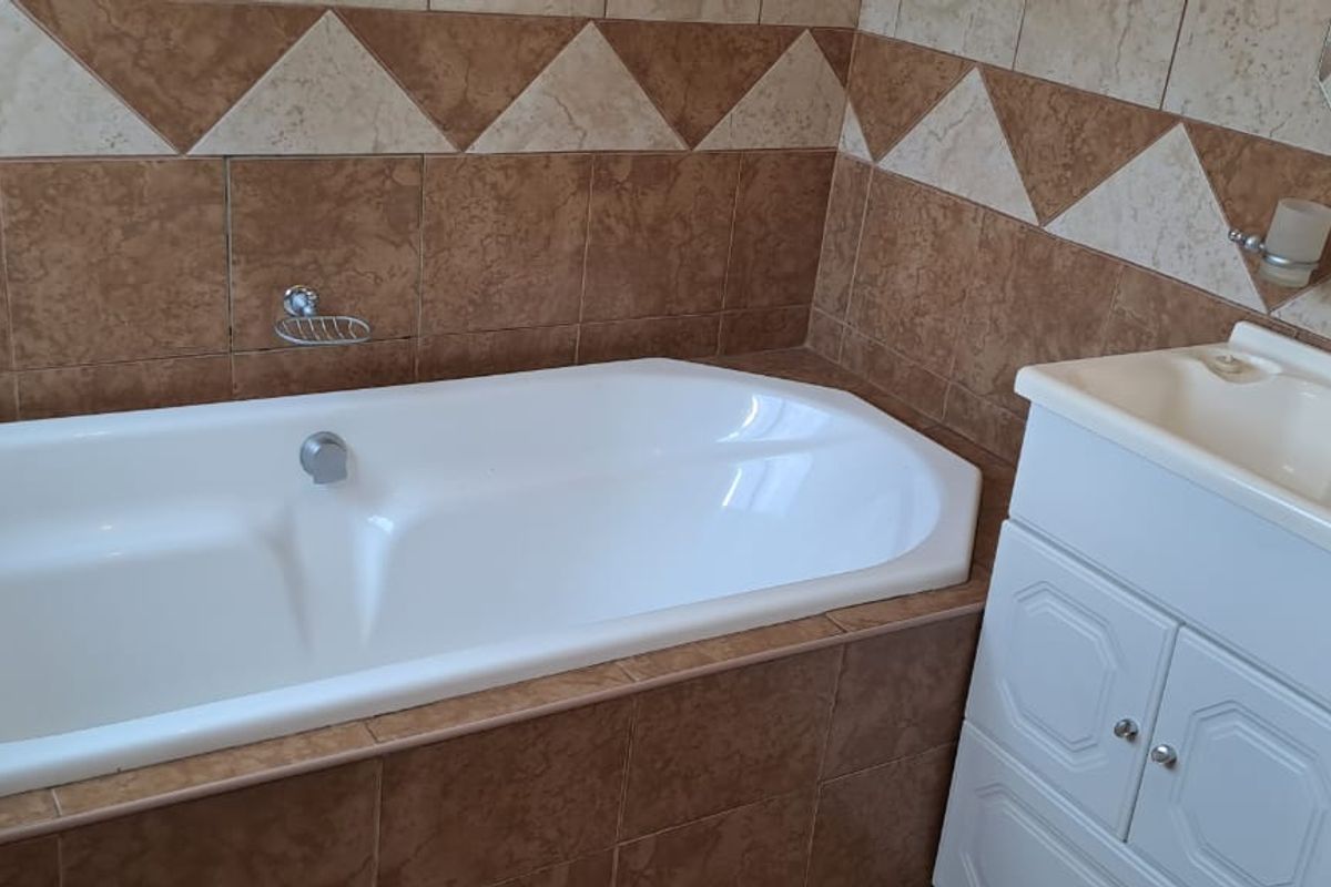 A functional bathroom featuring a built-in bathtub and a vanity cabinet with a basin, finished with decorative ceramic wall tiling.