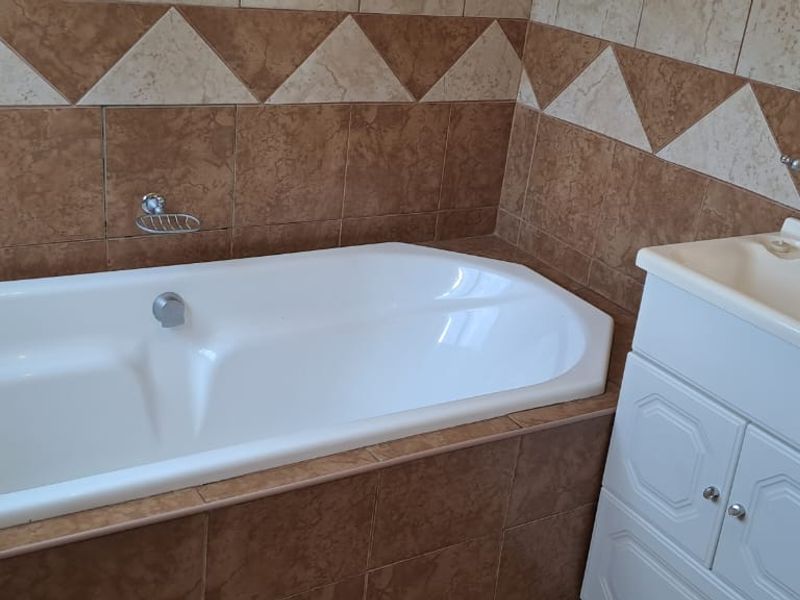 A functional bathroom featuring a built-in bathtub and a vanity cabinet with a basin, finished with decorative ceramic wall tiling.