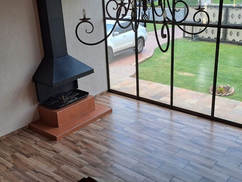Spacious living area featuring a built-in fireplace, wood-look tile flooring, and large floor-to-ceiling windows providing views of the garden.