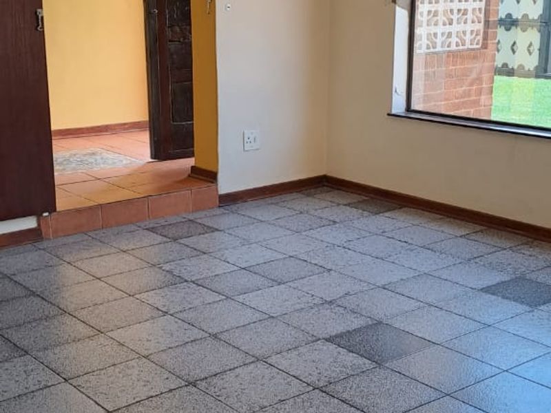An empty living room featuring tiled flooring, a sliding door leading to an adjacent space, and a window with views of the exterior.