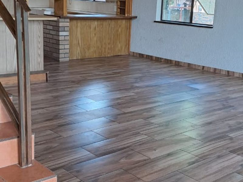 Spacious open-plan living area featuring wood-look tile flooring, a vaulted timber ceiling, and a built-in kitchen with a brick-base breakfast bar.