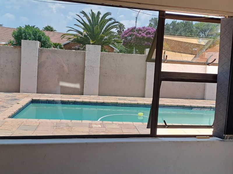 View from an interior room looking out onto a private swimming pool, paved pool deck, and surrounding boundary wall.