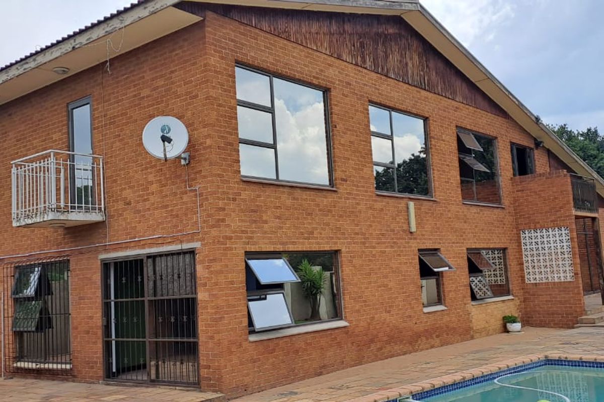 Rear view of a double-storey face brick house featuring a swimming pool, paved patio, and balcony access.