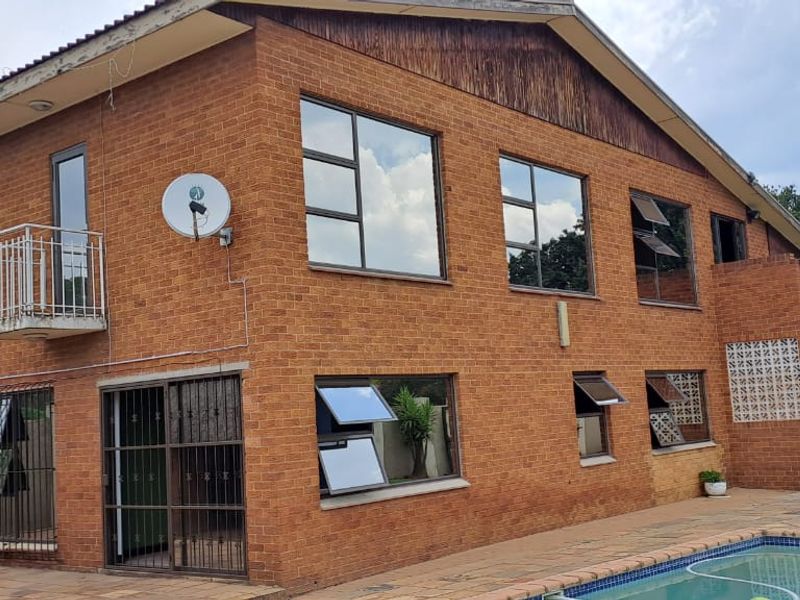 Rear view of a double-storey face brick house featuring a swimming pool, paved patio, and balcony access.