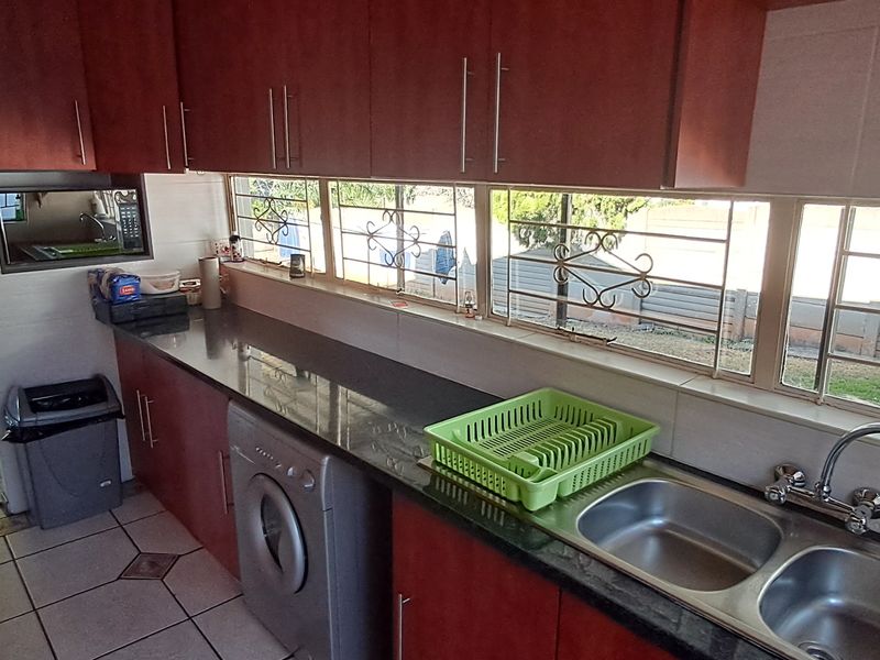 A functional kitchen featuring dark laminate cabinetry, granite countertops, a double bowl stainless steel sink, and tiled flooring with views to the exterior.