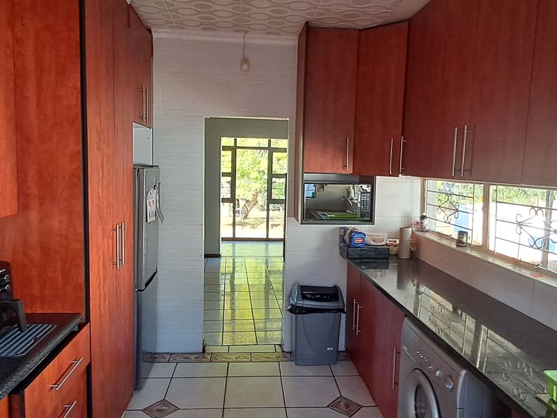 A functional kitchen featuring wood-finish cabinetry, dark granite countertops, tiled flooring, and an integrated extractor fan, with a view through to the rear entrance.