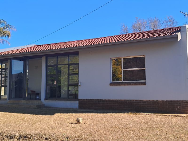 Rear view of a single-story house featuring a tiled roof, brick base, and large aluminium-framed windows and sliding doors.