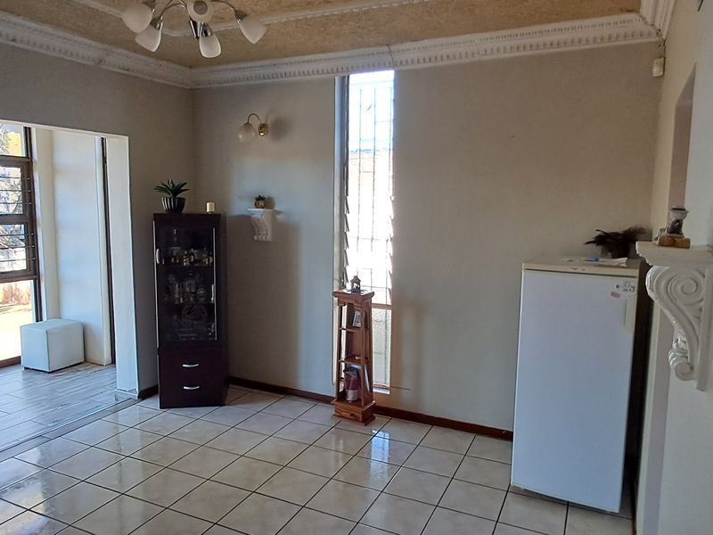 A living area featuring tiled flooring, decorative ceiling cornices, and louvered windows with security bars, offering a functional space with potential for modernization.
