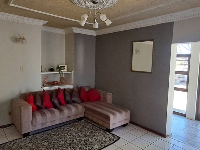 A living room featuring tiled floors, decorative ceiling cornices, a built-in wall niche, and direct access to the garden through a sliding glass door.