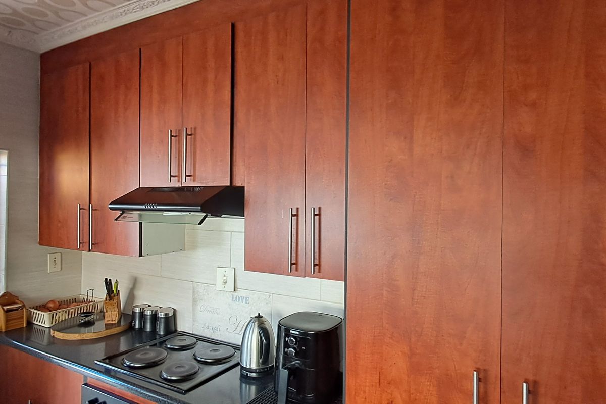 A functional kitchen featuring warm-toned wooden cabinetry, a built-in electric hob with an extractor fan, and a tiled backsplash.