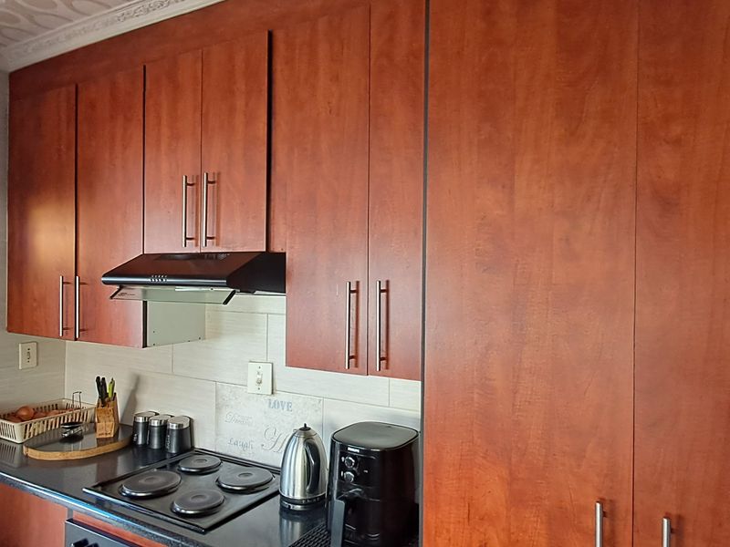 A functional kitchen featuring warm-toned wooden cabinetry, a built-in electric hob with an extractor fan, and a tiled backsplash.