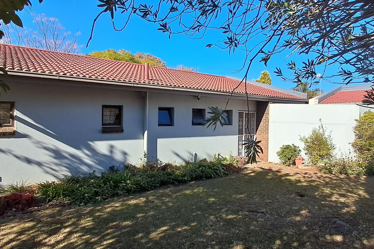 Rear view of the property featuring a tiled roof, plastered exterior walls, and a garden area with established landscaping.