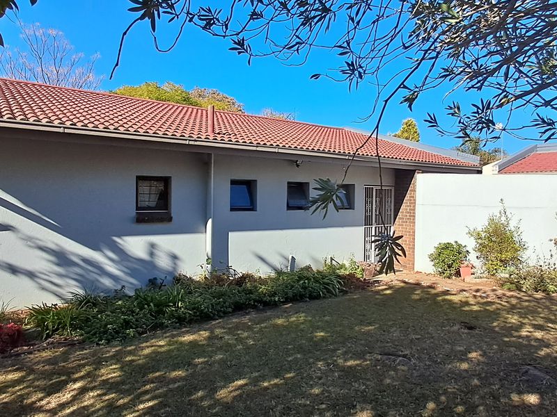 Rear view of the property featuring a tiled roof, plastered exterior walls, and a garden area with established landscaping.