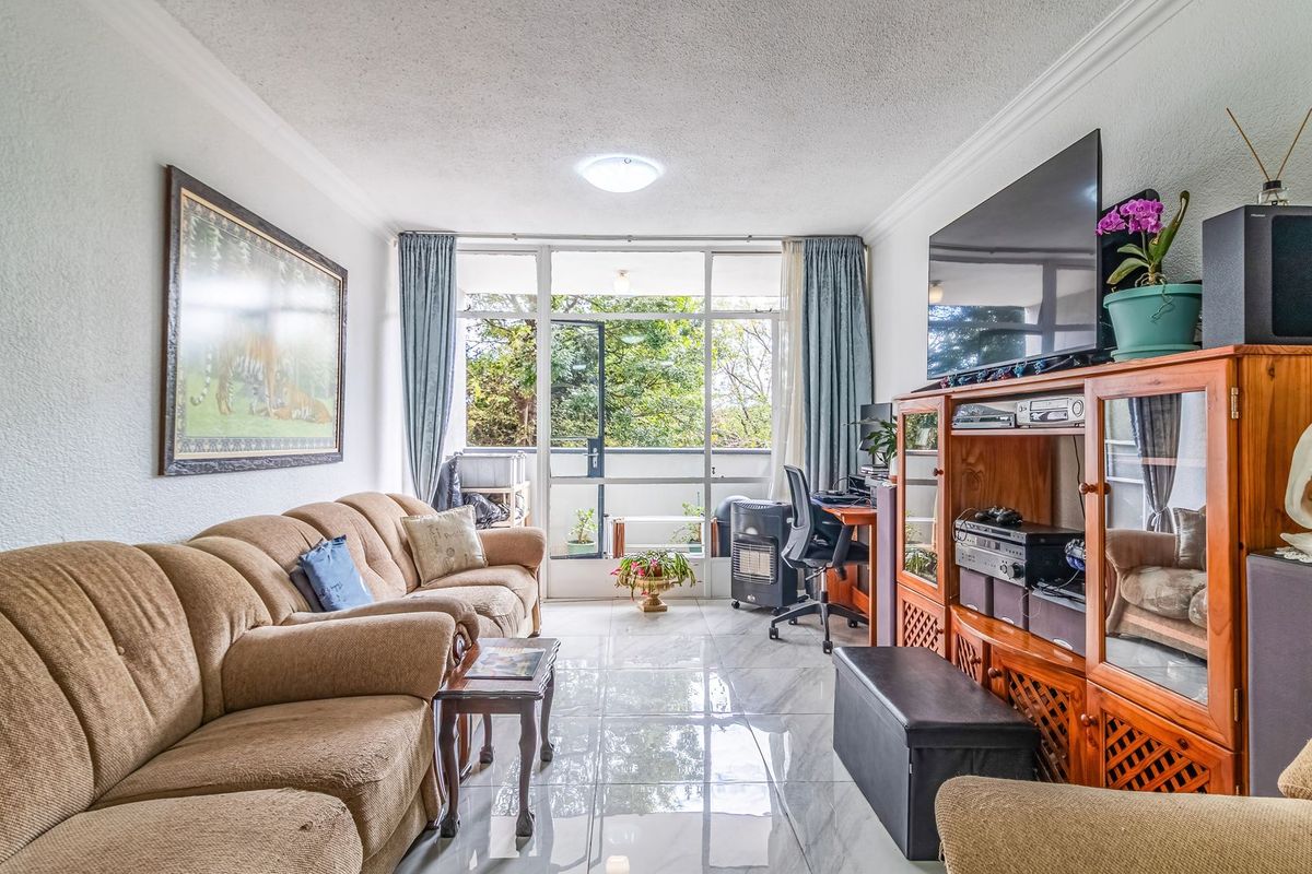 A bright living room featuring polished tiled flooring, ceiling cornicing, and a large sliding glass door providing access to an outdoor balcony area.
