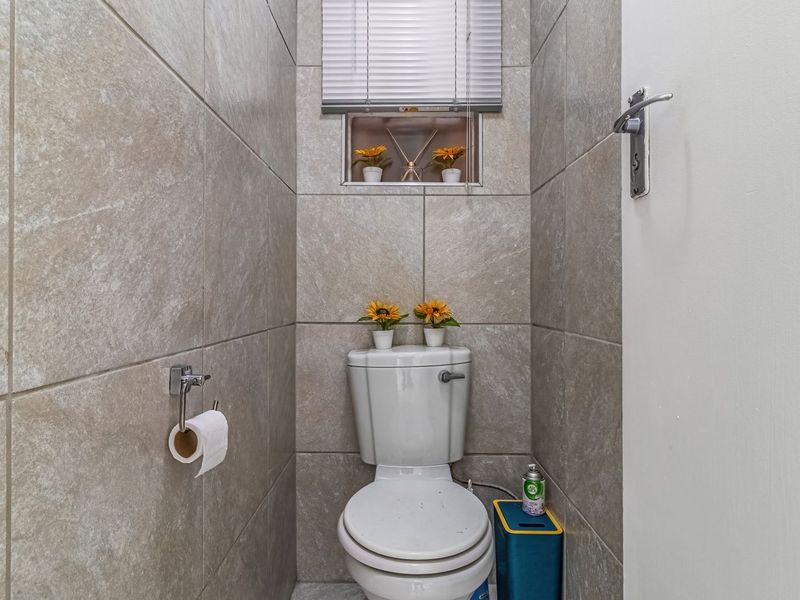 A compact guest bathroom featuring neutral ceramic wall tiles, a standard toilet, and a small window with a fitted blind.