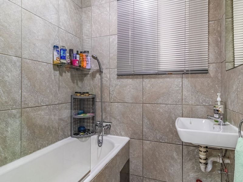 A compact bathroom featuring full-height wall tiling, a bathtub with a handheld shower attachment, and a wall-mounted basin.