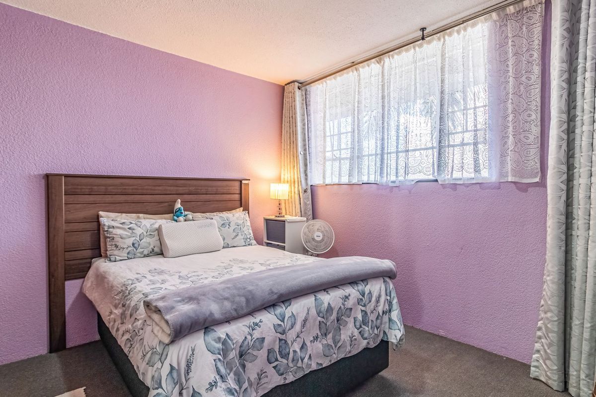 A bedroom featuring textured purple walls, carpeted flooring, and a built-in wardrobe, offering a functional space with natural light from the window.