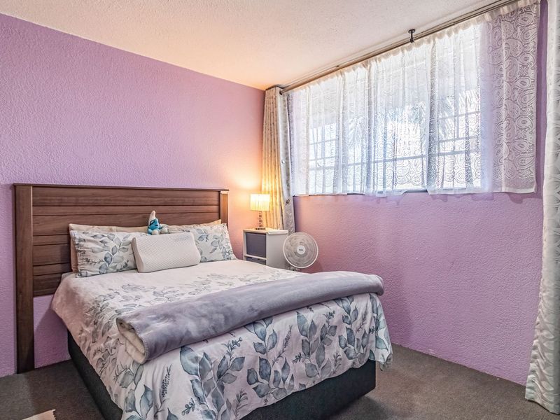 A bedroom featuring textured purple walls, carpeted flooring, and a built-in wardrobe, offering a functional space with natural light from the window.