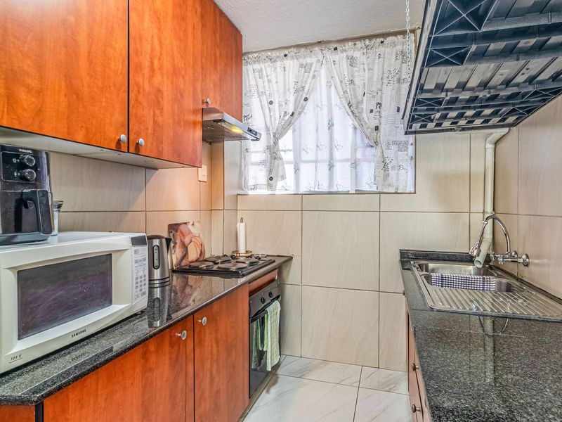 Compact kitchen featuring granite countertops, wooden cabinetry, built-in oven, gas hob, and a stainless steel sink with tiled finishes.