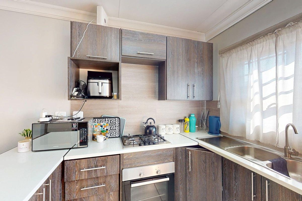 A functional kitchen featuring wood-grain laminate cabinetry, a gas hob, built-in oven, and a stainless steel sink with a tiled backsplash.