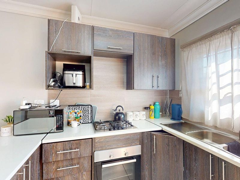 A functional kitchen featuring wood-grain laminate cabinetry, a gas hob, built-in oven, and a stainless steel sink with a tiled backsplash.