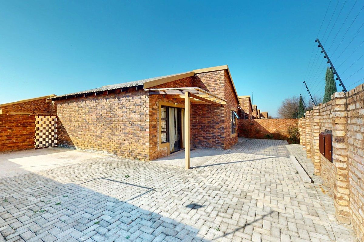 A rear exterior view of a face brick house featuring a paved courtyard, a timber pergola, and secure perimeter electric fencing.