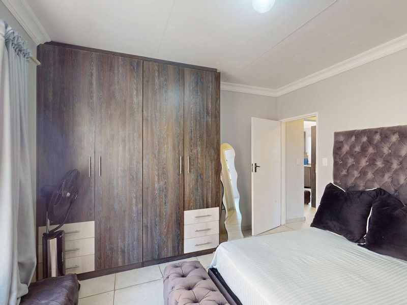 A well-maintained bedroom featuring extensive built-in wooden cupboards, neutral tiled flooring, and classic ceiling cornicing.
