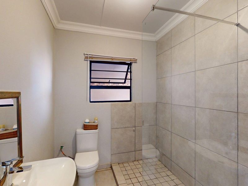 A clean, modern bathroom featuring a walk-in shower with a glass screen, neutral wall tiling, and a pedestal basin.
