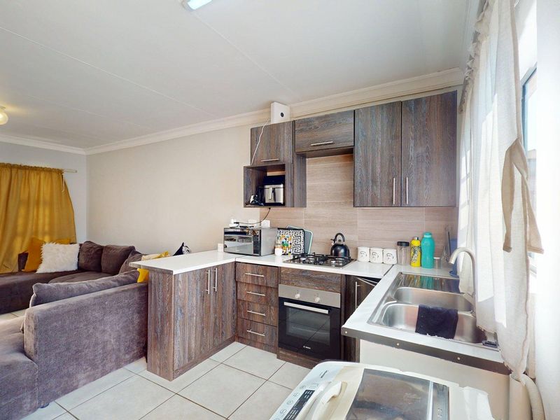 Open-plan kitchen and living area featuring wood-look cabinetry, gas hob, electric oven, and tiled flooring, creating a functional and connected living space.
