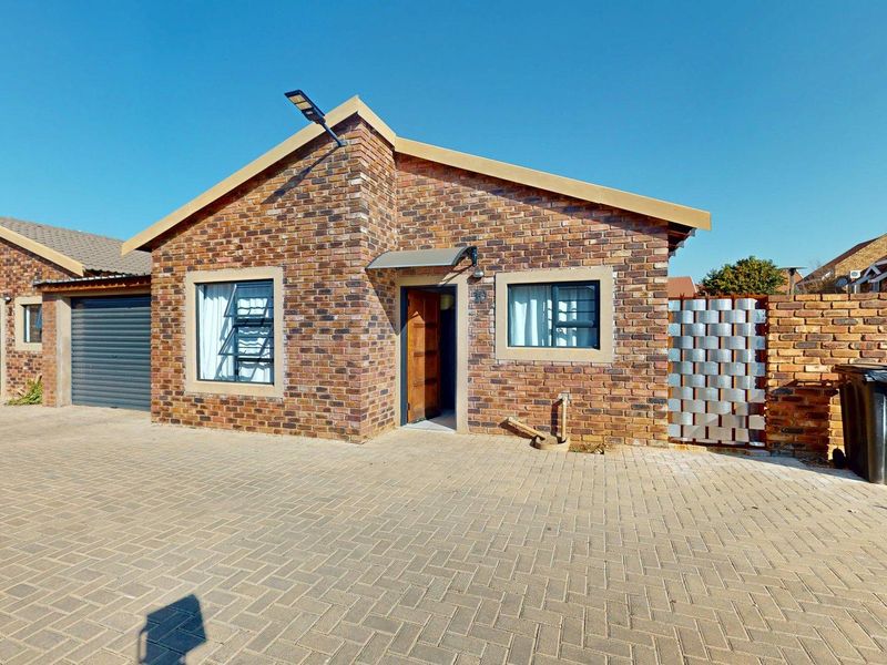 Front elevation of a face brick house featuring a paved driveway, single garage, and secure entrance with a metal privacy screen.